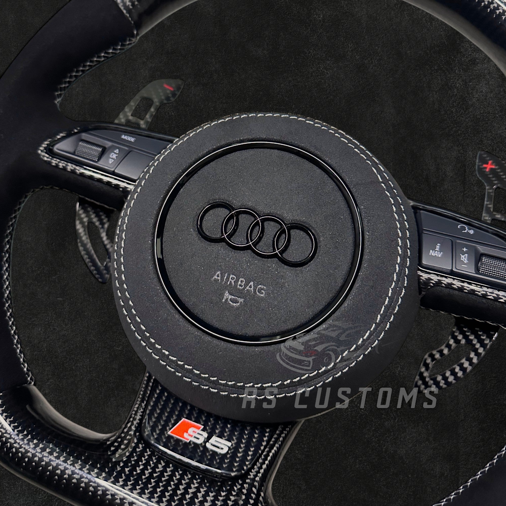 RS CUSTOMS Audi RS steering wheel with carbon fiber, Alcantara, and white stitching. Features a white racing stripe at 12 o'clock.