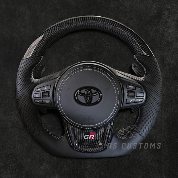 RS Customs Toyota GR Supra MK5 custom steering wheel with carbon fiber, perforated leather grips and optional custom airbag cover for A90 and A91 Supra models.