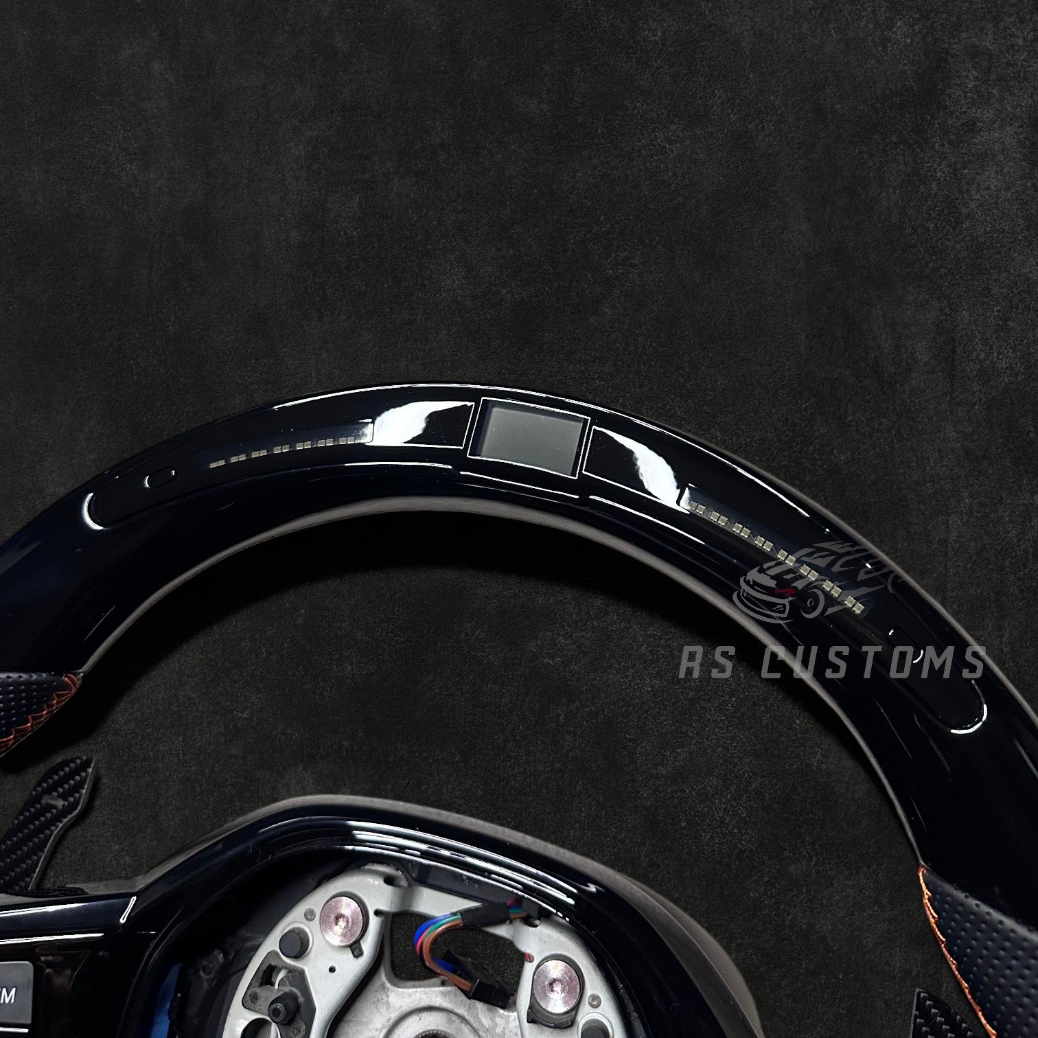 RS CUSTOMS BMW G-Series custom steering wheel with piano black trim, perforated leather grips, and orange stitching. Features LED display.