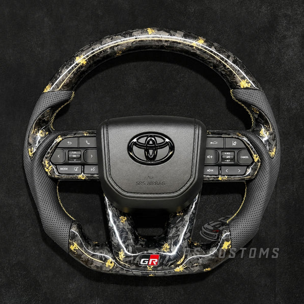 RS CUSTOMS Toyota Land Cruiser GR steering wheel with forged carbon fiber, colored flakes, perforated leather grips, and GR logo.