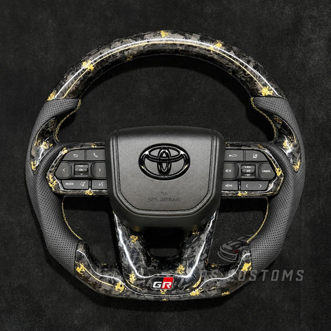 RS CUSTOMS Toyota Land Cruiser GR steering wheel with forged carbon fiber, colored flakes, perforated leather grips, and GR logo.