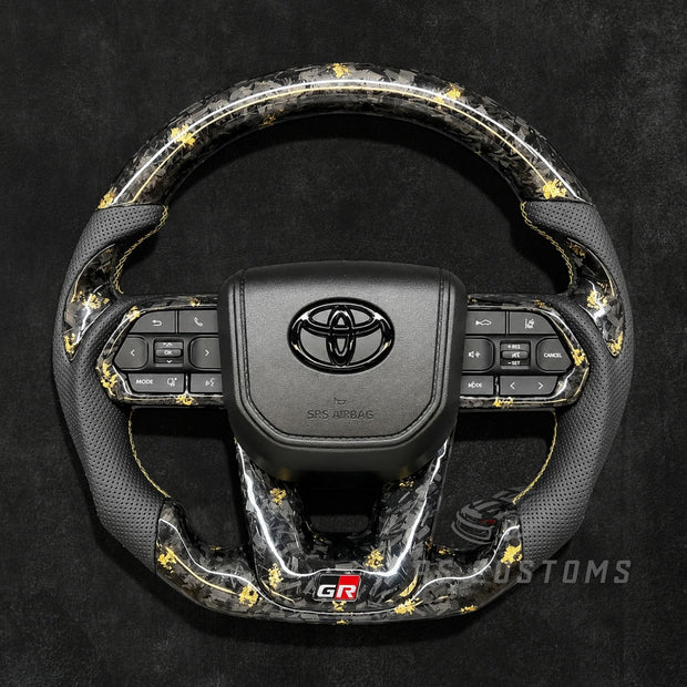 RS CUSTOMS Toyota Land Cruiser GR steering wheel with forged carbon fiber, colored flakes, perforated leather grips, and GR logo.